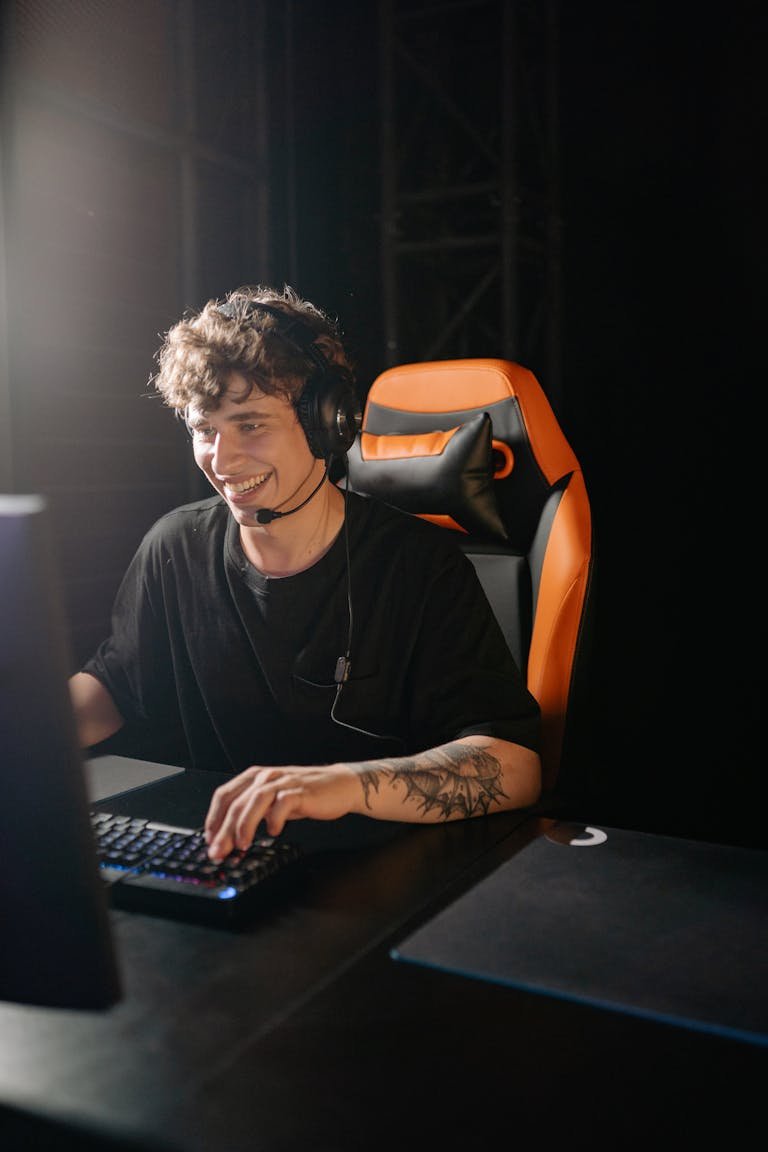 Smiling young man playing games on PC with headphones, enjoying a thrilling gaming session.
